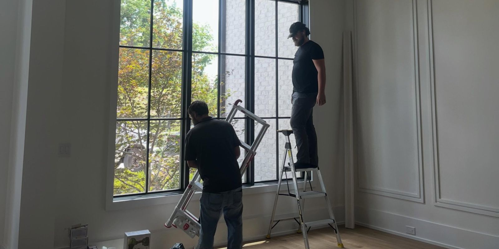 Two Brentwood Blind Company installers at a tall window, setting up for an installation